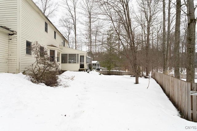 yard layered in snow featuring a sunroom and fence