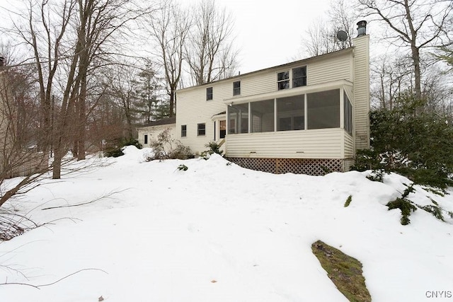 snow covered back of property with a sunroom and a chimney