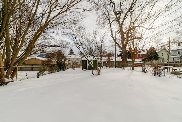 yard covered in snow with a residential view, a fenced backyard, an outdoor structure, and a shed