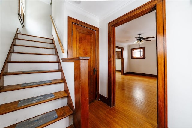 staircase with baseboards, ornamental molding, ceiling fan, and wood finished floors