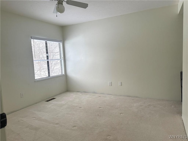 carpeted spare room featuring visible vents, a textured ceiling, and a ceiling fan