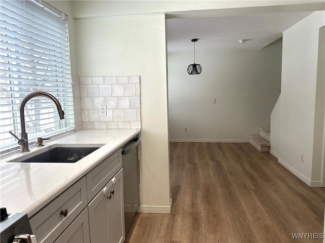 kitchen with wood finished floors, a sink, light countertops, dishwasher, and backsplash