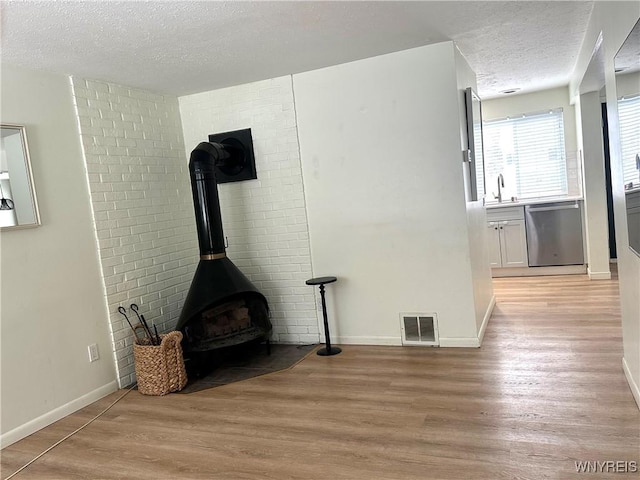 unfurnished living room with baseboards, visible vents, light wood finished floors, a wood stove, and a textured ceiling