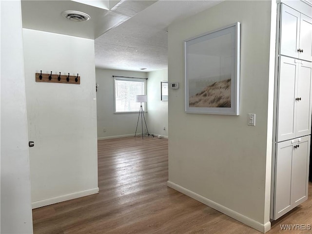 hall with a textured ceiling, wood finished floors, visible vents, and baseboards