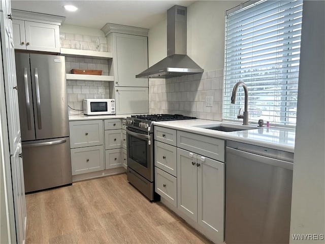 kitchen featuring wall chimney range hood, light countertops, light wood-style flooring, appliances with stainless steel finishes, and a sink