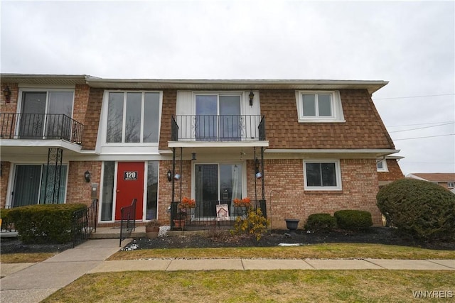 townhome / multi-family property with a shingled roof, mansard roof, and brick siding