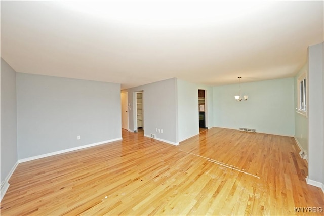 empty room featuring light wood-style floors, visible vents, baseboards, and an inviting chandelier