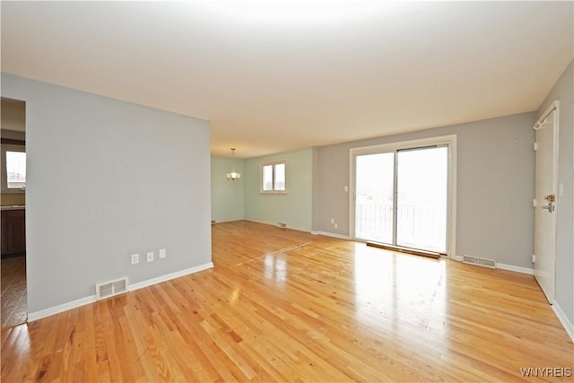 spare room with light wood finished floors, baseboards, visible vents, and an inviting chandelier