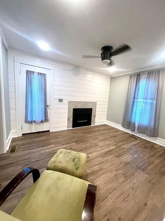 living area with a tiled fireplace, wood finished floors, a ceiling fan, and baseboards