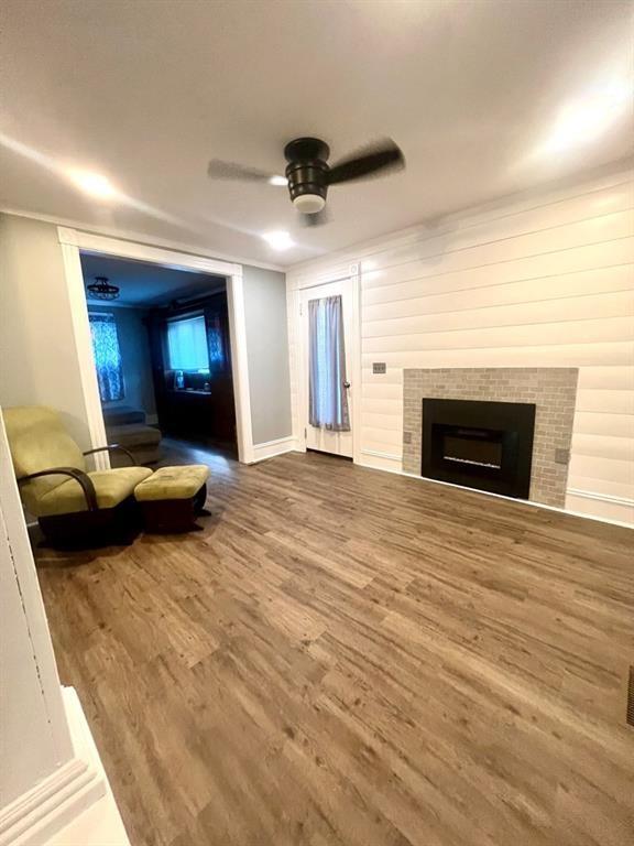 unfurnished living room featuring ceiling fan, a fireplace, baseboards, and wood finished floors