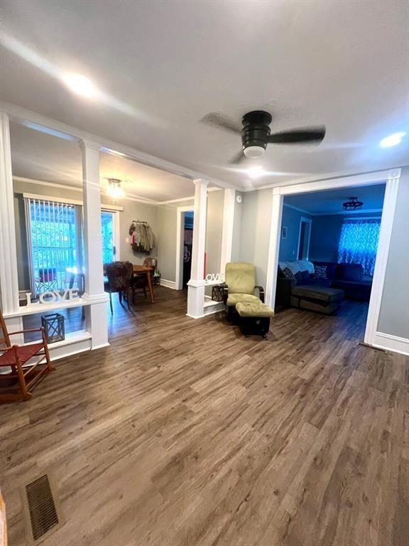 sitting room featuring ceiling fan, wood finished floors, visible vents, baseboards, and decorative columns