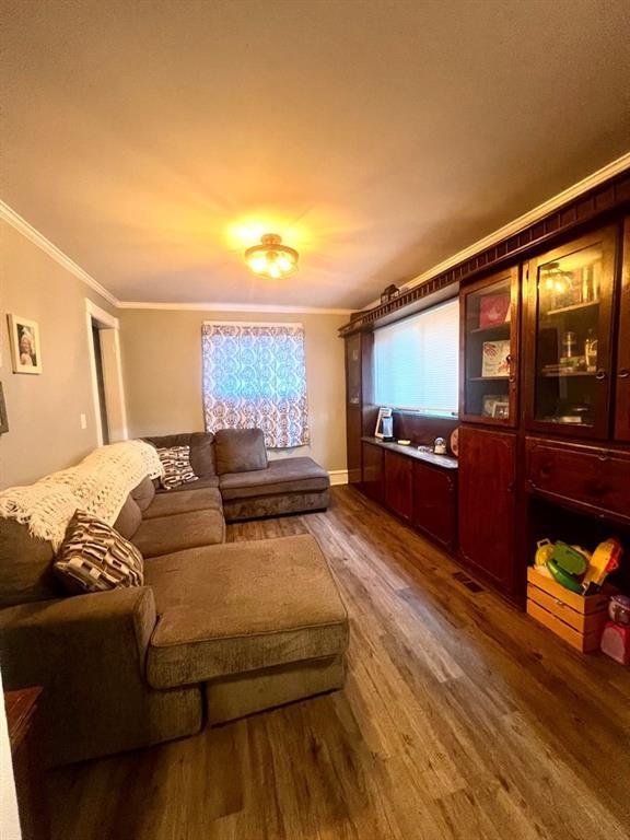 living area with ornamental molding, visible vents, and wood finished floors