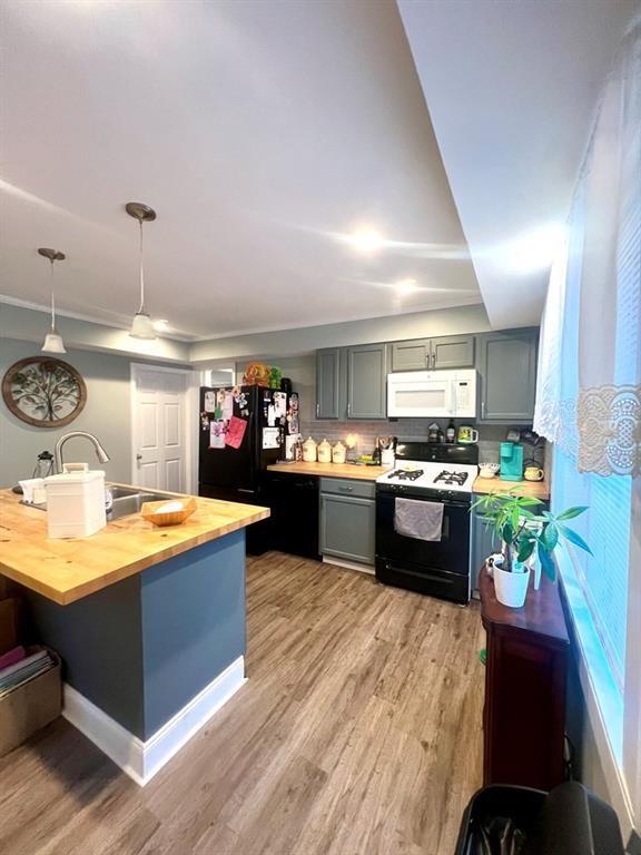 kitchen with gas range, white microwave, freestanding refrigerator, gray cabinetry, and wooden counters