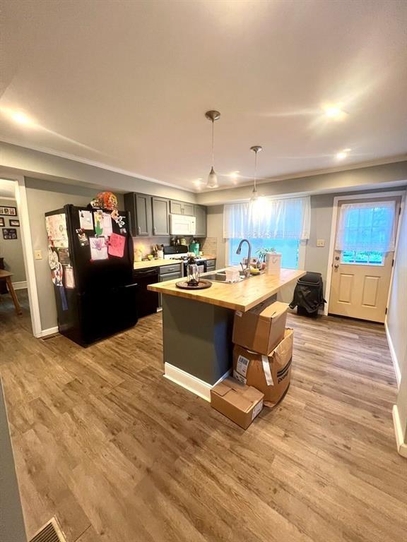 kitchen with a center island with sink, wood finished floors, black appliances, wooden counters, and a sink