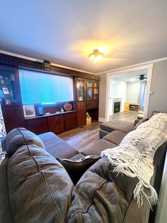 living area with a tiled fireplace, ornamental molding, and wood finished floors