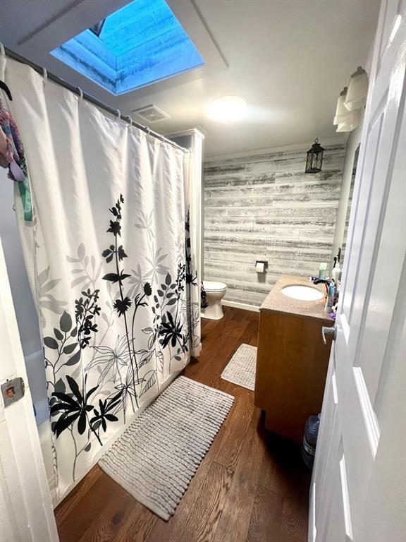 bathroom featuring a skylight, crown molding, toilet, vanity, and wood finished floors