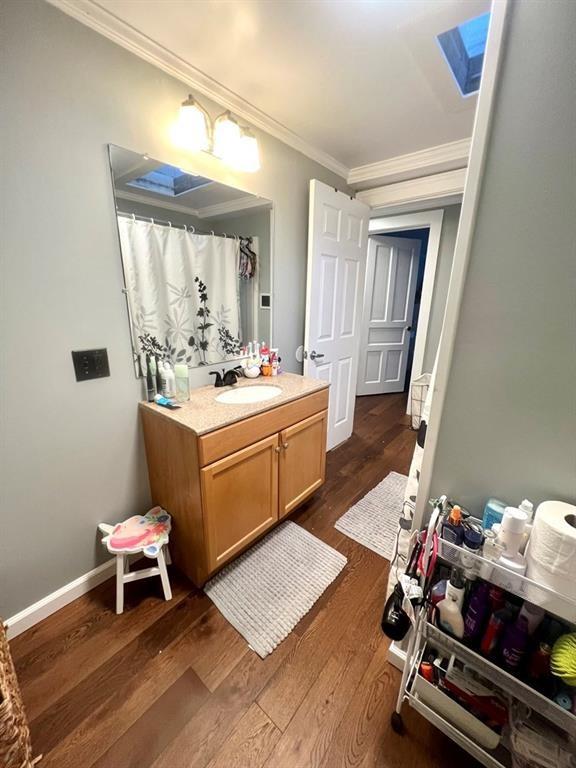 bathroom featuring a skylight, baseboards, ornamental molding, wood finished floors, and vanity