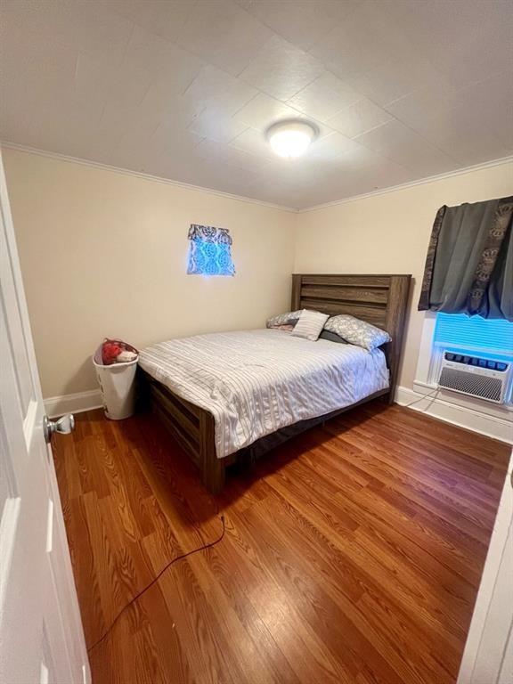 unfurnished bedroom featuring baseboards, cooling unit, wood finished floors, and crown molding