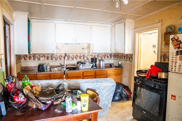 kitchen featuring brown cabinetry, white cabinets, black gas range oven, freestanding refrigerator, and a sink