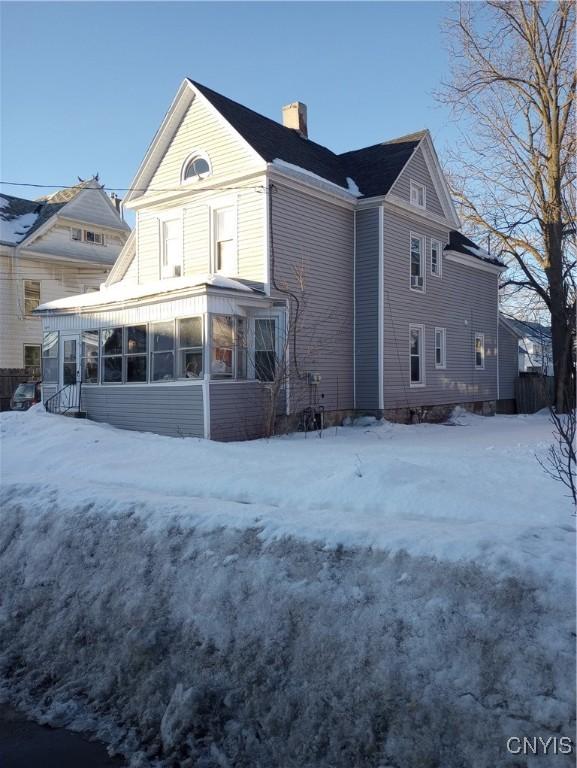 snow covered property featuring a chimney and a sunroom