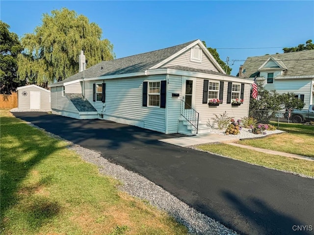 view of front facade with a storage unit, entry steps, fence, an outdoor structure, and a front lawn