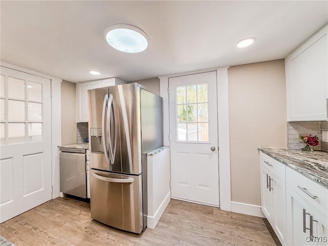 kitchen featuring light wood-style flooring, light stone counters, appliances with stainless steel finishes, white cabinetry, and backsplash