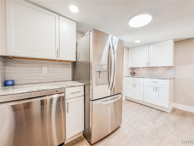 kitchen with light stone counters, white cabinetry, appliances with stainless steel finishes, light wood-type flooring, and decorative backsplash