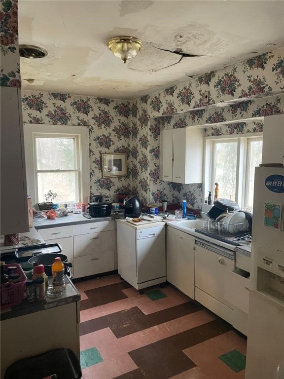 kitchen featuring dishwashing machine, white cabinets, freestanding refrigerator, light floors, and wallpapered walls