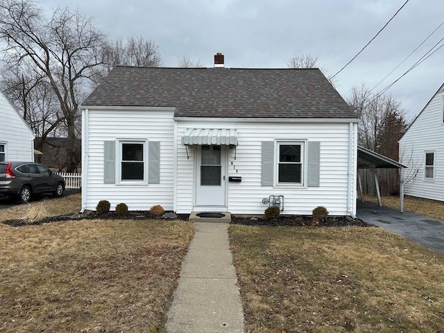 view of front of property featuring a shingled roof, a chimney, an attached carport, aphalt driveway, and a front lawn