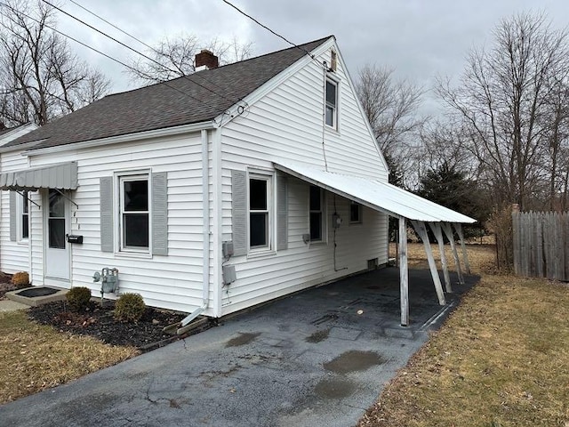 view of side of property with a chimney, aphalt driveway, roof with shingles, fence, and a carport