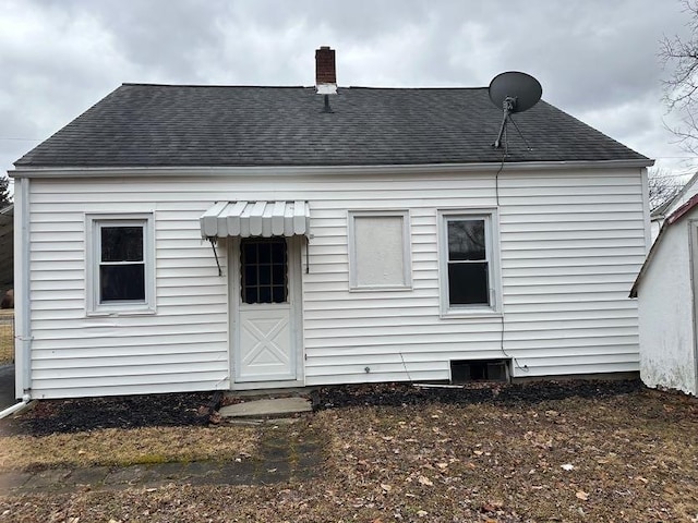 rear view of house with roof with shingles and a chimney