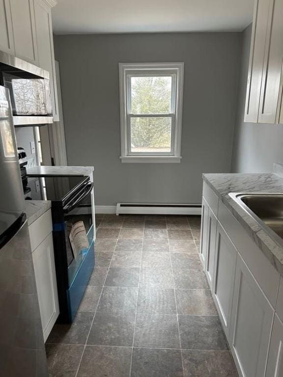 kitchen featuring light countertops, baseboard heating, appliances with stainless steel finishes, white cabinetry, and baseboards