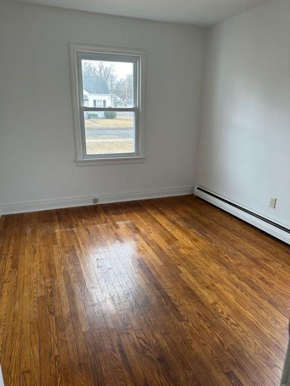 spare room featuring baseboard heating, baseboards, and hardwood / wood-style flooring