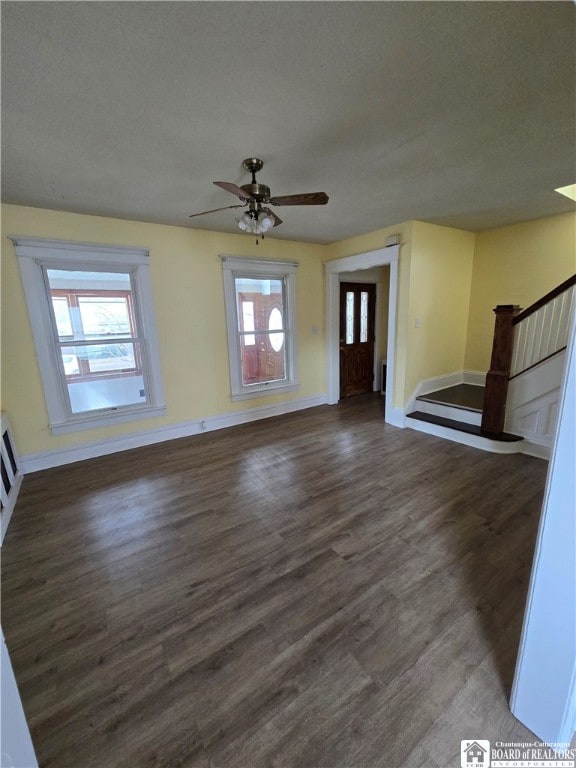 unfurnished living room featuring a ceiling fan, stairs, baseboards, and wood finished floors