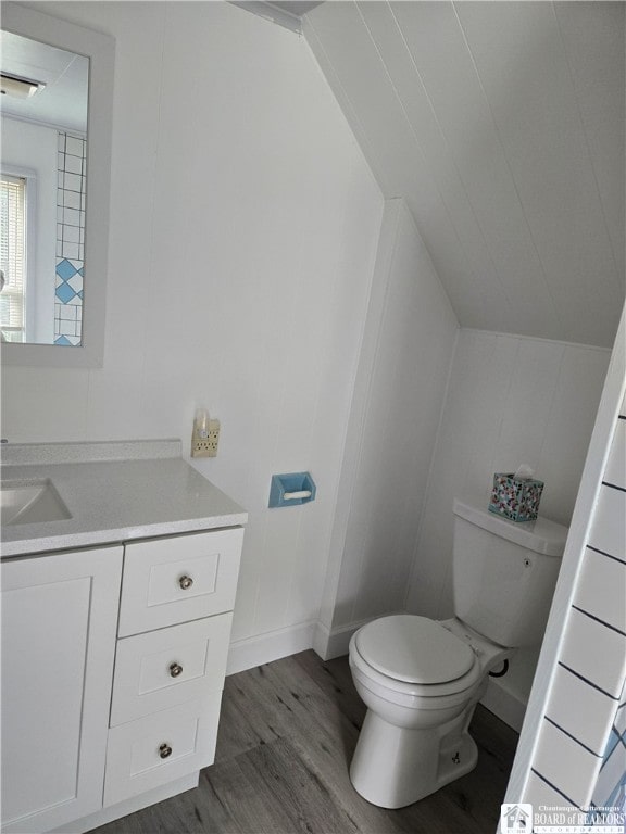 half bathroom featuring lofted ceiling, toilet, vanity, wood finished floors, and baseboards