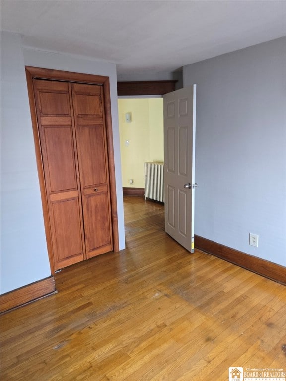 unfurnished bedroom featuring radiator, light wood-style floors, baseboards, and a closet