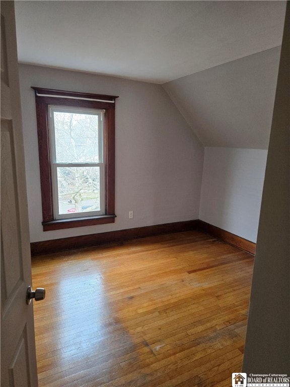 additional living space with light wood-type flooring, baseboards, and vaulted ceiling