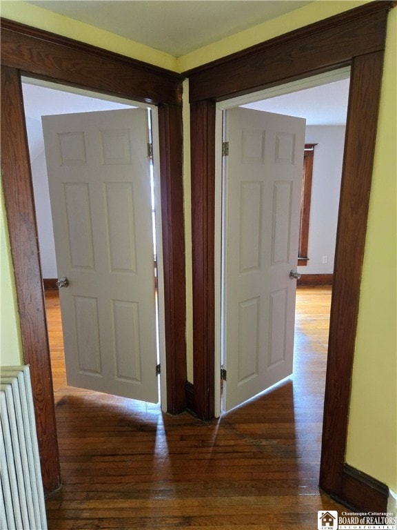 corridor with radiator heating unit, wood finished floors, and baseboards