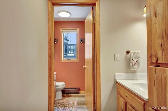 half bath with a baseboard heating unit, vanity, toilet, and wood finished floors