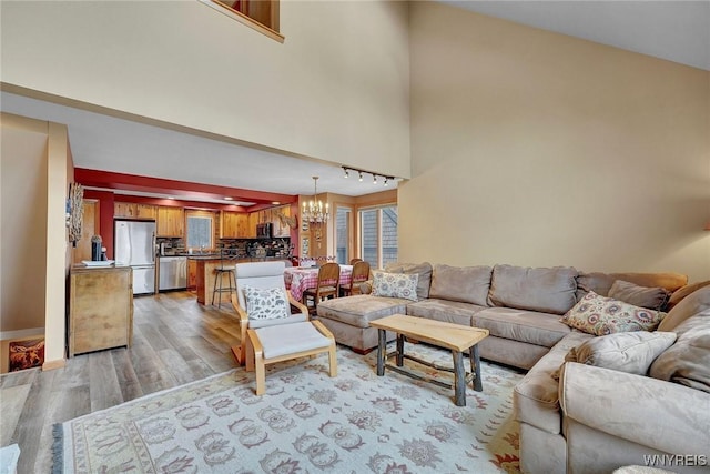 living area with a chandelier, a high ceiling, light wood-type flooring, and track lighting