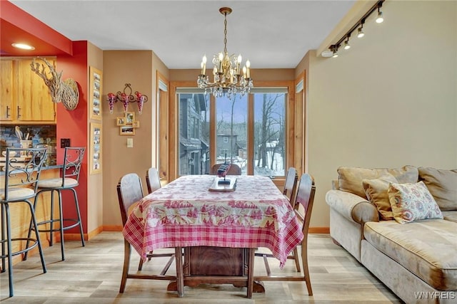 dining area featuring a chandelier, light wood finished floors, rail lighting, and baseboards