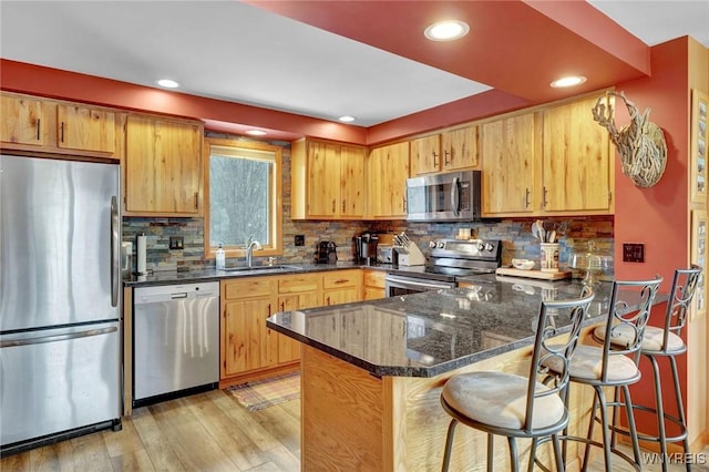 kitchen featuring light wood finished floors, tasteful backsplash, appliances with stainless steel finishes, a sink, and a peninsula