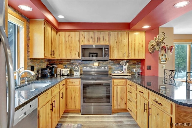 kitchen with stainless steel appliances, a peninsula, a sink, dark stone counters, and tasteful backsplash