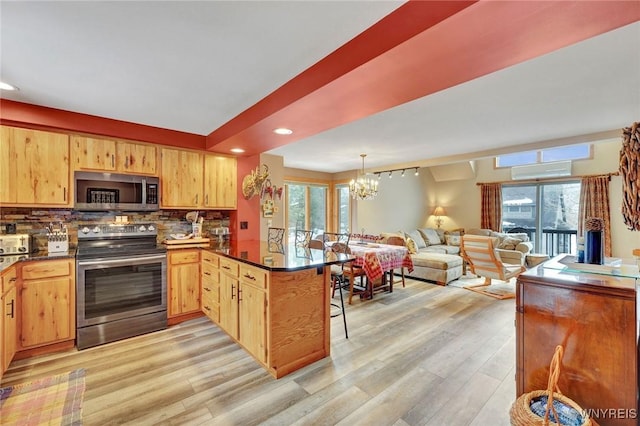 kitchen with a breakfast bar, backsplash, appliances with stainless steel finishes, light wood-style floors, and a peninsula