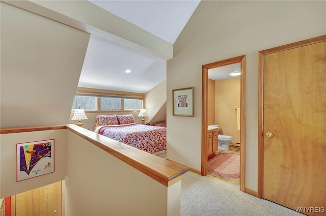 bedroom with lofted ceiling, baseboards, light colored carpet, and ensuite bath