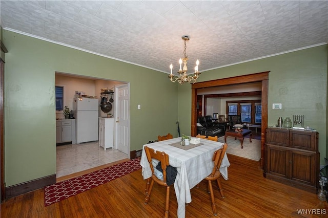 dining room featuring a notable chandelier, crown molding, baseboards, and wood finished floors