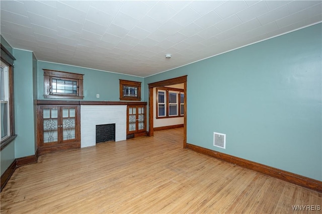 unfurnished living room featuring light wood-style floors, visible vents, a fireplace, and baseboards