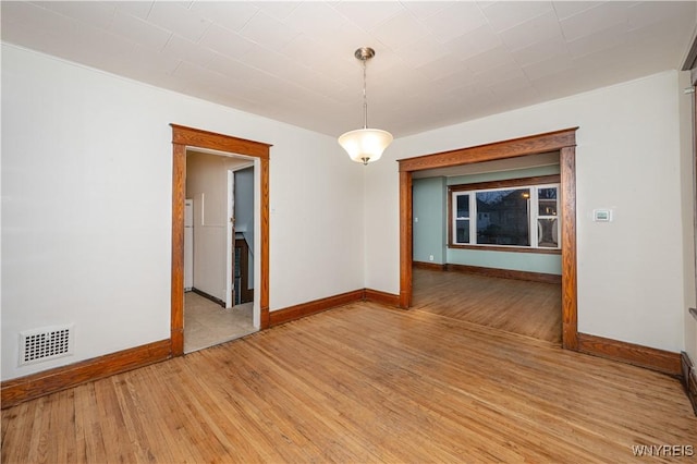 empty room featuring light wood finished floors, visible vents, and baseboards