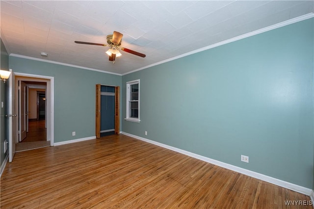 spare room featuring crown molding, wood finished floors, a ceiling fan, and baseboards