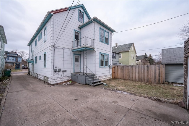 back of property featuring a balcony, driveway, and fence